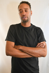 African American male in a black t-shirt looks into the camera with folded arms. 