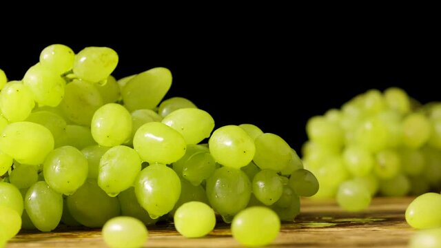 A bunch of green ripe grapes with water drops, rotating on a black studio background. Grapevine in drops of moisture. Wet berries of juicy grapes. Autumn harvest of sweet fruits. Close up. Slow motion