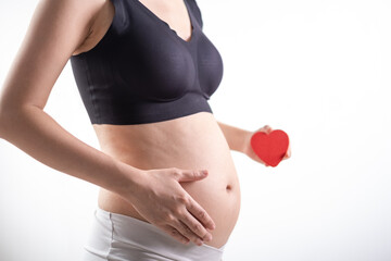 Pregnant woman in white and black underwear. Young woman expecting a baby. Side view hand holding red heart.