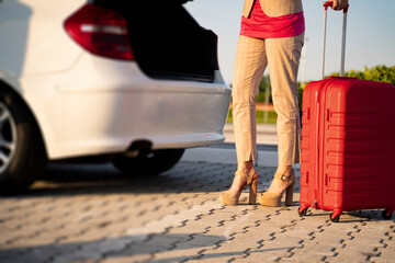 Unrecongnizable stilish woman in high heels putitng her luggage in the car trunk 