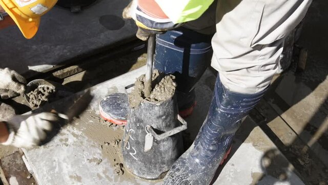Man In Boots Tamping Concrete In A Slump Cone With Steel Tamping Rod. high angle