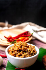 Sambal Peda, Indonesian Traditional Food in white bowl decorated with chiles and tomatoes on wooden table and golden cloth