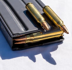 A rifle magazine loaded with 223 caliber bullets with two additional bullets on top of it on a white background