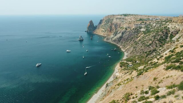 Aerial view of calm azure sea and volcanic rocky cliffs of Mys Fiolent. Pleasure trip boats moored in the bay. Nature summer ocean sea beach background. Holiday, vacation and travel concept