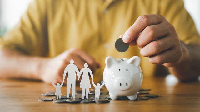 businessman putting coin on the piggybank and paper family on table, donation, saving, charity, family finance plan concept, fundraising, superannuation, investment, financial crisis concept.