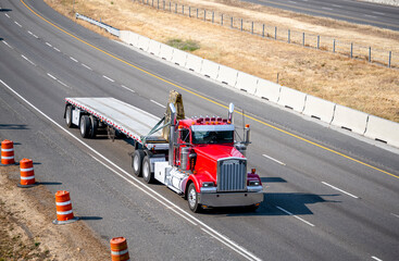 Classic powerful industrial red big rig semi truck transporting cargo fastened on flat bed semi...
