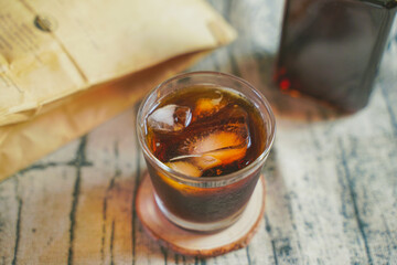 A glass of ice brewed coffee with paper bag beside