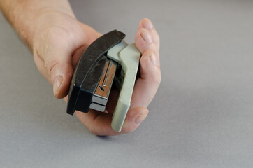 Hand and stapler on gray background. A man holding a plastic paper stapler. Part of a series. Close-up. Selective focus.