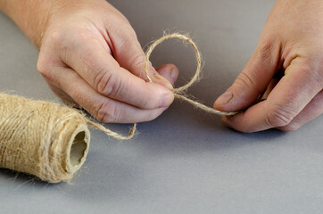 Two hands tie a knot of twine on a gray background. Quiver is a thin thread that is made by...