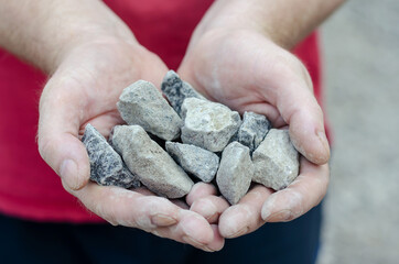 The man holds the rubble in his palms. Pieces of random granite stones. Close-up. Selective focus....