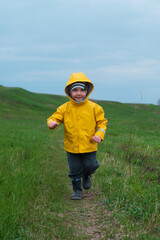 A blond boy in a yellow jacket runs in a green meadow