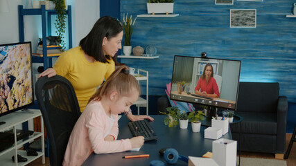 Child and mother using video call with teacher for online lesson and remote education. Young girl...