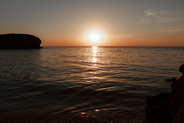 waves wash the rocky shore of the sea. Sunset. Reflection in the water of the bridge and rays