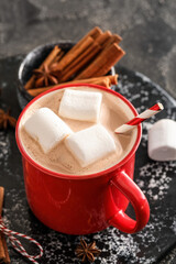 Board with cup of hot cocoa drink and spices on dark background, closeup