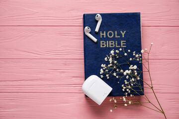 Holy Bible, earphones and gypsophila flowers on pink wooden background