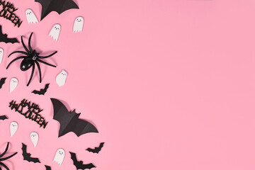 Halloween flat lay with bats, spiders, Happy Halloween text and cute ghosts on side of pink background with copy space