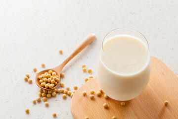 soy milk in glass with soy beans on spoon on stone table.