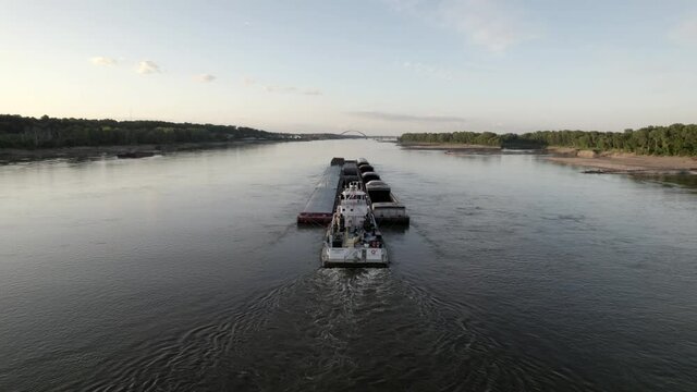 Aerial descent behind tugboat pushing barges on Mississippi River, St. Louis.