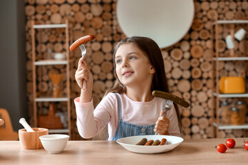 Cute little girl with tasty sausages in kitchen