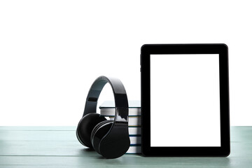Modern headphones, tablet computer and books on color wooden table against white background