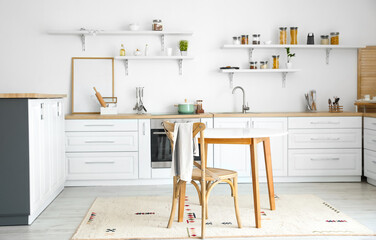 Interior of modern stylish kitchen with blank poster frame and dining table