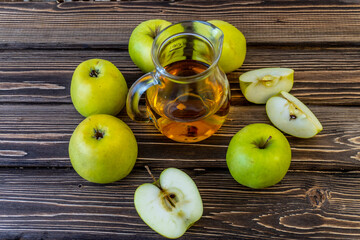 Green apples and jug with apple juice on wooden background