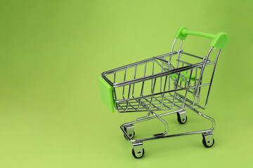 An empty mini supermarket trolley on green backround