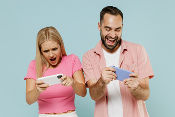 Gambling young couple two friends family man woman in casual clothes using play racing app mobile cell phone hold gadget smartphone pc video games together isolated on plain blue background studio.