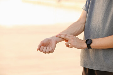 Sporty male runner checking pulse outdoors