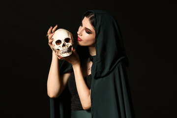 Young witch with human skull on dark background