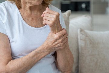 Close-up elderly woman suffering from arthritis of the hands sitting on the couch. The concept of...