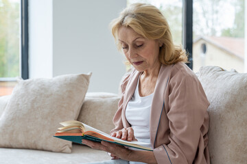 Elderly woman resting at living room. She is reading novel 