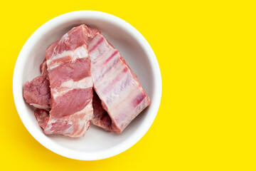 Raw pork ribs in white bowl on yellow background.