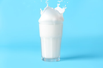 Glass of tasty milk with splashes on blue background