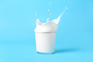 Glass of tasty milk with splashes on blue background