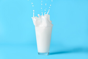 Glass of milk splashing on color background