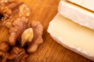 Sliced camembert and walnut kernels on a wooden cutting board, close-up, selective focus.