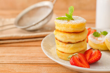 Plate with cottage cheese pancakes and strawberries on wooden background