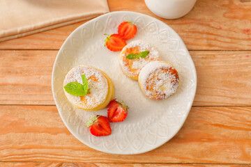 Plate with cottage cheese pancakes and strawberries on wooden background