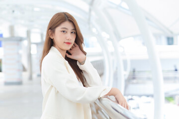 Portrait with blur background of long hair beautiful Asian professional woman in white suit with smiling face posing while working outside the office.