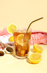 Glass of refreshing Long Island iced tea with lemon, sunglasses and towel on color background