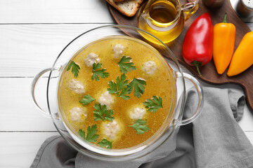 Pot with tasty meatball soup, vegetables and spices on light wooden background