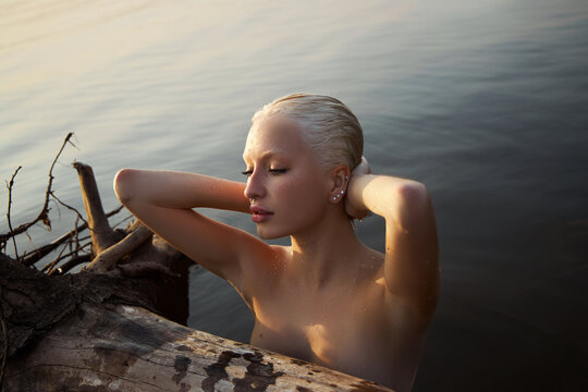Nude naked sexy woman in water at sunset. Beautiful blonde woman with short wet hair and big breasts, art portrait in sea