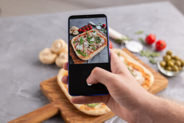 Male photographing on smartphone pizza with ham and mushrooms. Social networks and delivery food application concept.