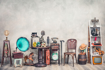 Antique gramophone, chair, old typewriter, retro radio, tape recorder, projector, books, clock, camera, fiddle, mask, cylinder hat, cowboy boots, bow, cane, suitcase. Vintage style filtered photo