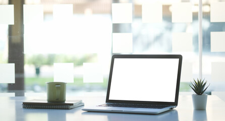 Mock up computer laptop with empty display and coffee cup on white table in modern office.