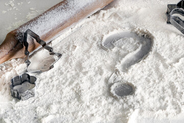 Question mark drawn on scattered flour on table with wooden rolling pin and Christmas baking molds....