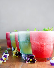 Delicious healthy kiwi and strawbeery, raspberry smoothies served with fresh mint in glasses on rustic wooden table.