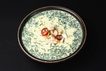 Summer cold yogurt soup okroshka with chicken served in a blue bowl over black background.
