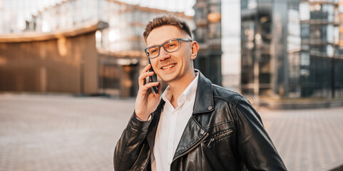 Handsome man with glasses with a smartphone on the street of a big city. Businessman talking on the phone on urban background